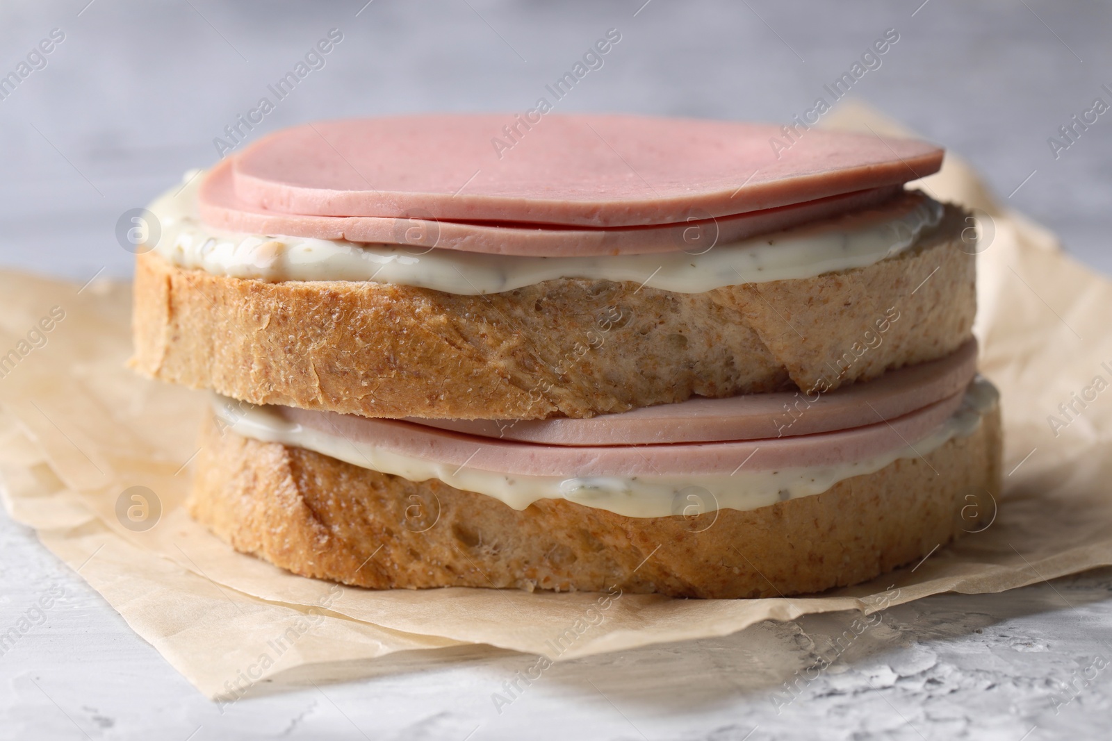 Photo of Delicious sandwich with boiled sausage and sauce on grey textured table, closeup