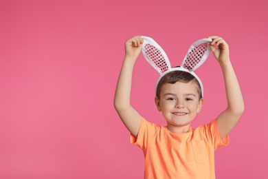 Portrait of little boy in Easter bunny ears headband on color background, space for text