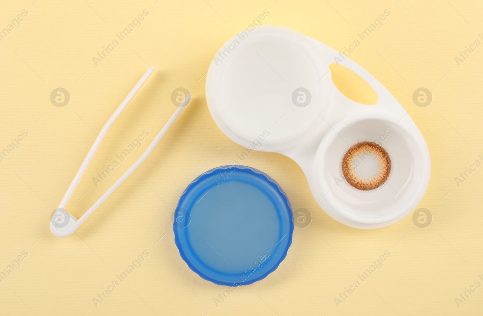 Photo of Case with color contact lenses and tweezers on pale yellow background, flat lay