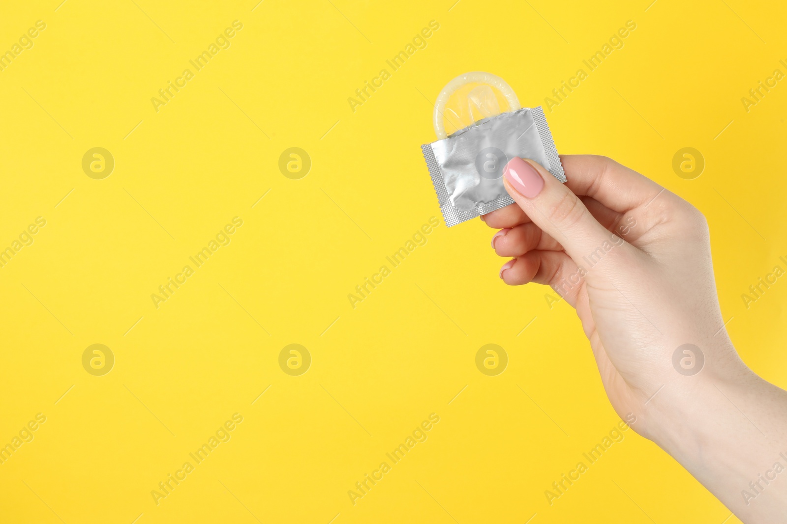 Photo of Woman holding condom on yellow background, closeup. Space for text