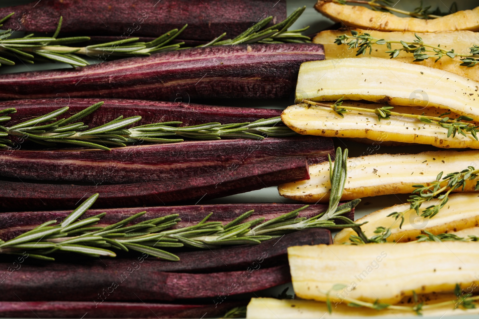 Photo of Raw white and black cut carrots with herbs as background, closeup