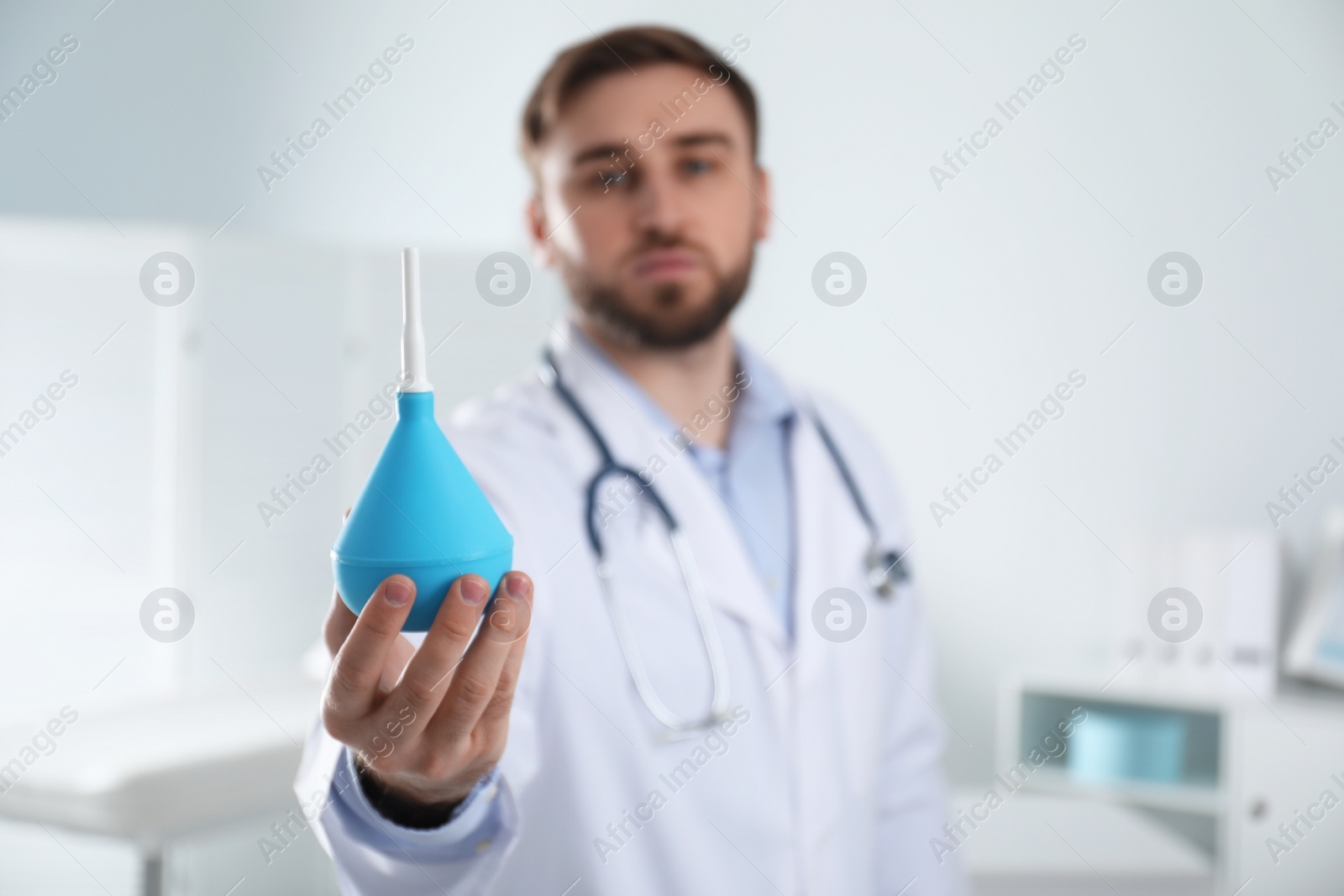 Photo of Doctor holding rubber enema in examination room, focus on hand. Space for text