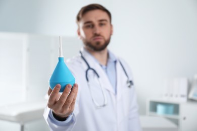 Doctor holding rubber enema in examination room, focus on hand. Space for text