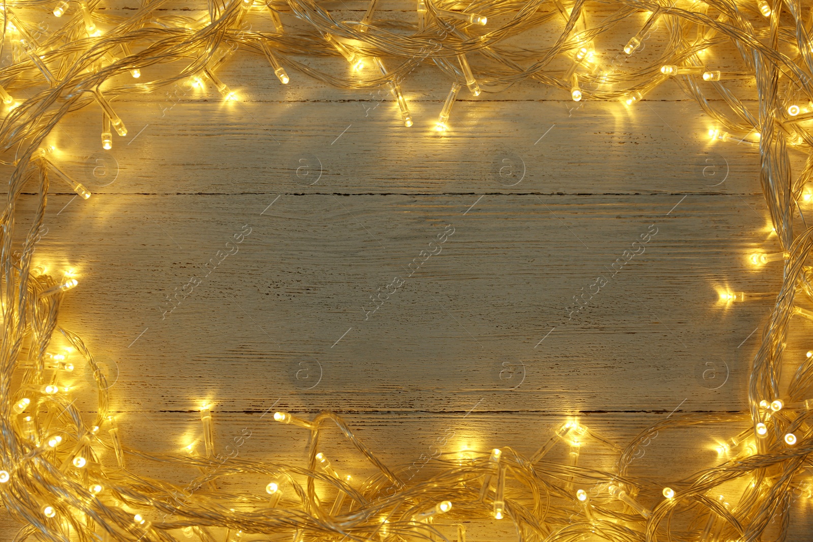 Photo of Frame made of glowing Christmas lights on white wooden background, top view. Space for text