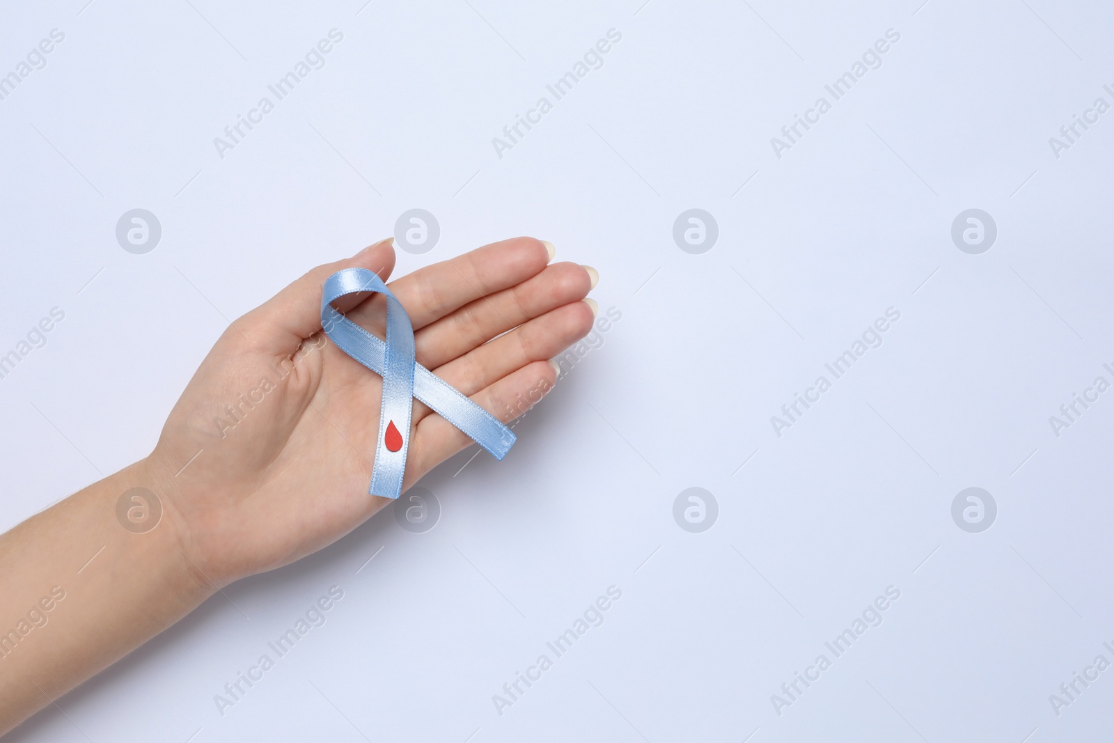 Photo of Woman holding light blue ribbon with drop of blood on white background, top view. Diabetes awareness