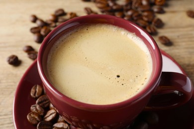 Photo of Cup of hot aromatic coffee and roasted beans on wooden table, closeup