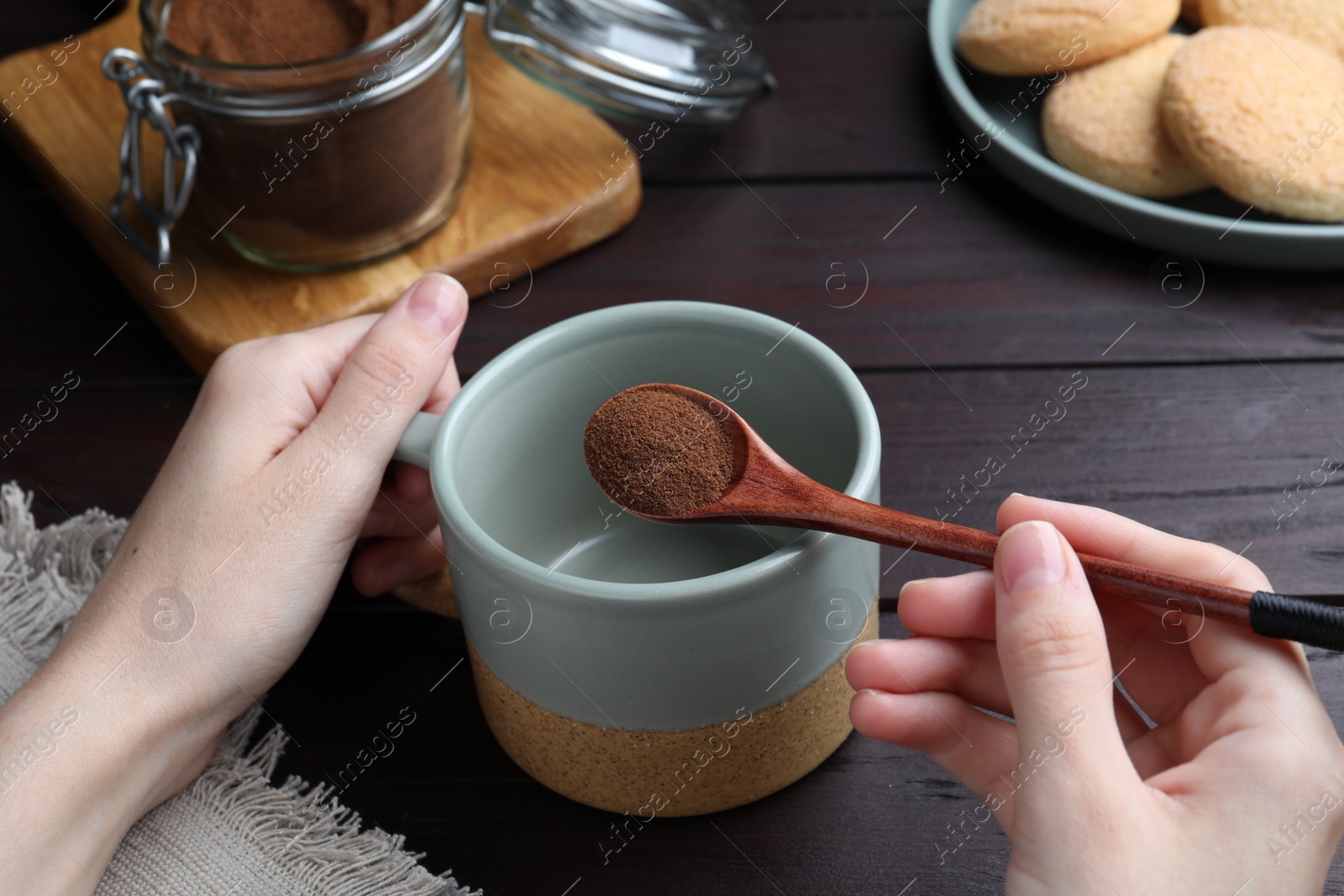 Photo of Woman pouring instant coffee into mug at wooden table, closeup