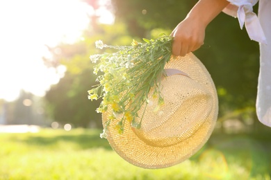 Young woman with straw hat and bouquet outdoors on sunny day, closeup