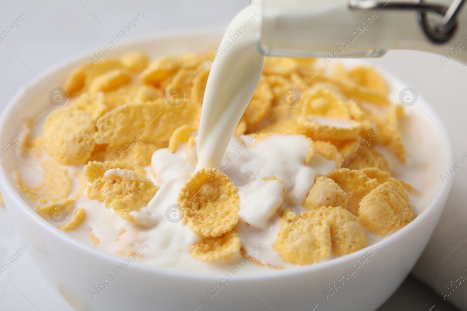 Photo of Breakfast cereal. Pouring milk into bowl with tasty corn flakes at table, closeup