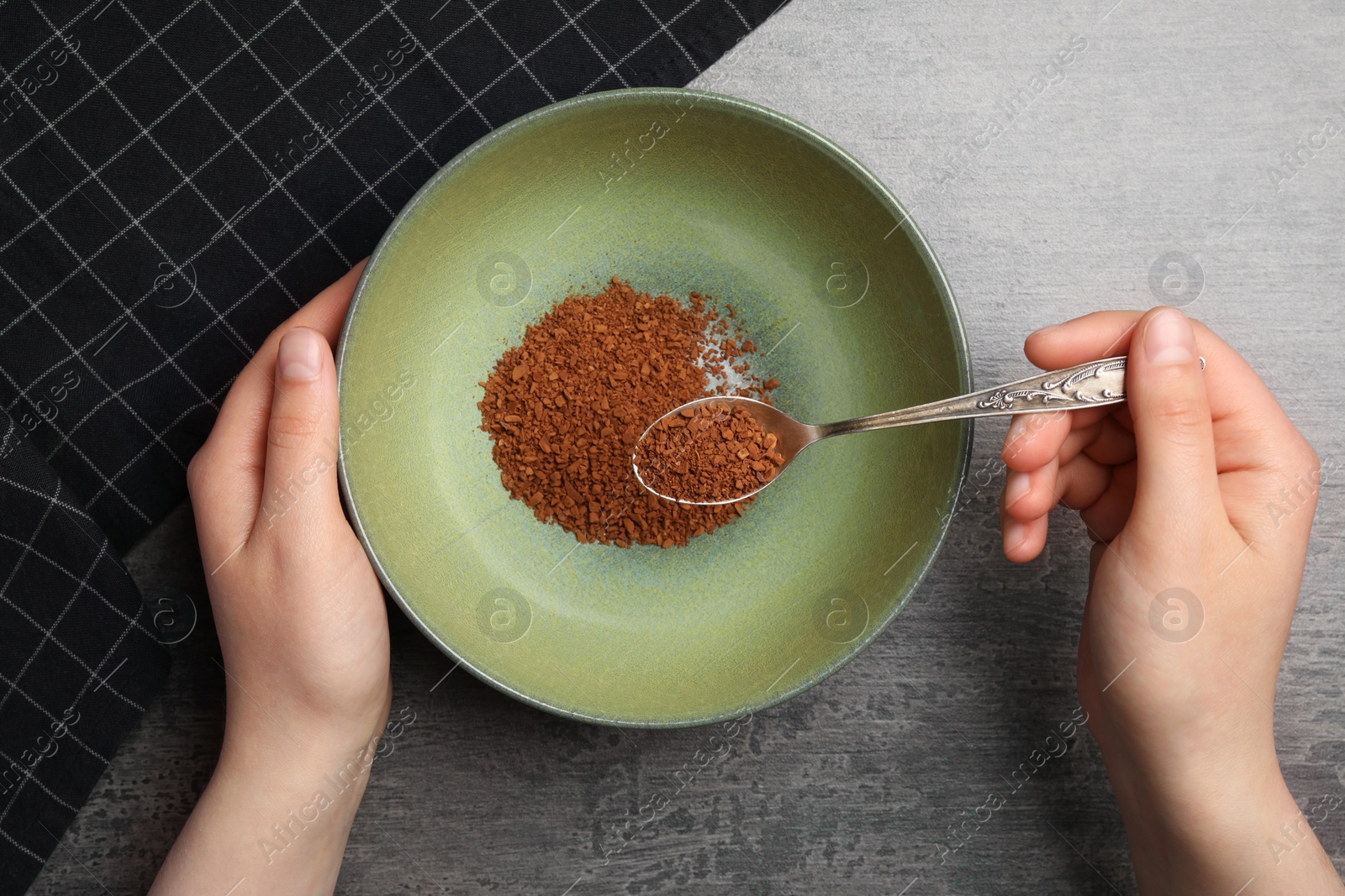 Photo of Woman pouring instant coffee granules into bowl at gray table, top view