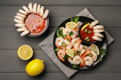 Tasty boiled shrimps with cocktail sauce, chili, parsley and lemon on grey wooden table, flat lay