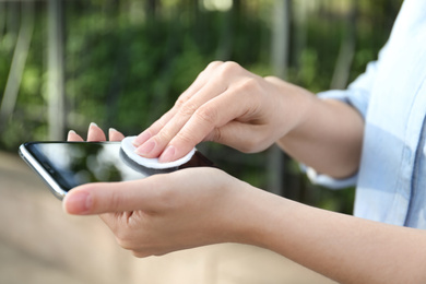 Photo of Woman cleaning smartphone with cotton pad outdoors, closeup