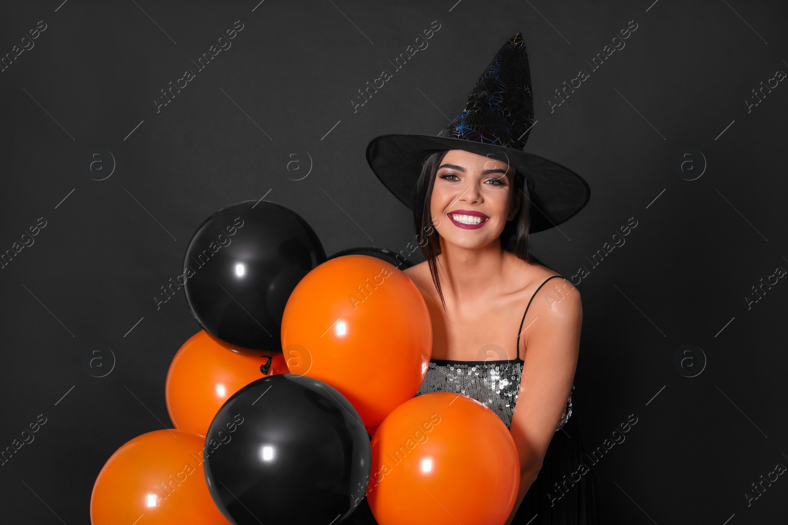 Photo of Beautiful woman wearing witch costume with balloons for Halloween party on black background