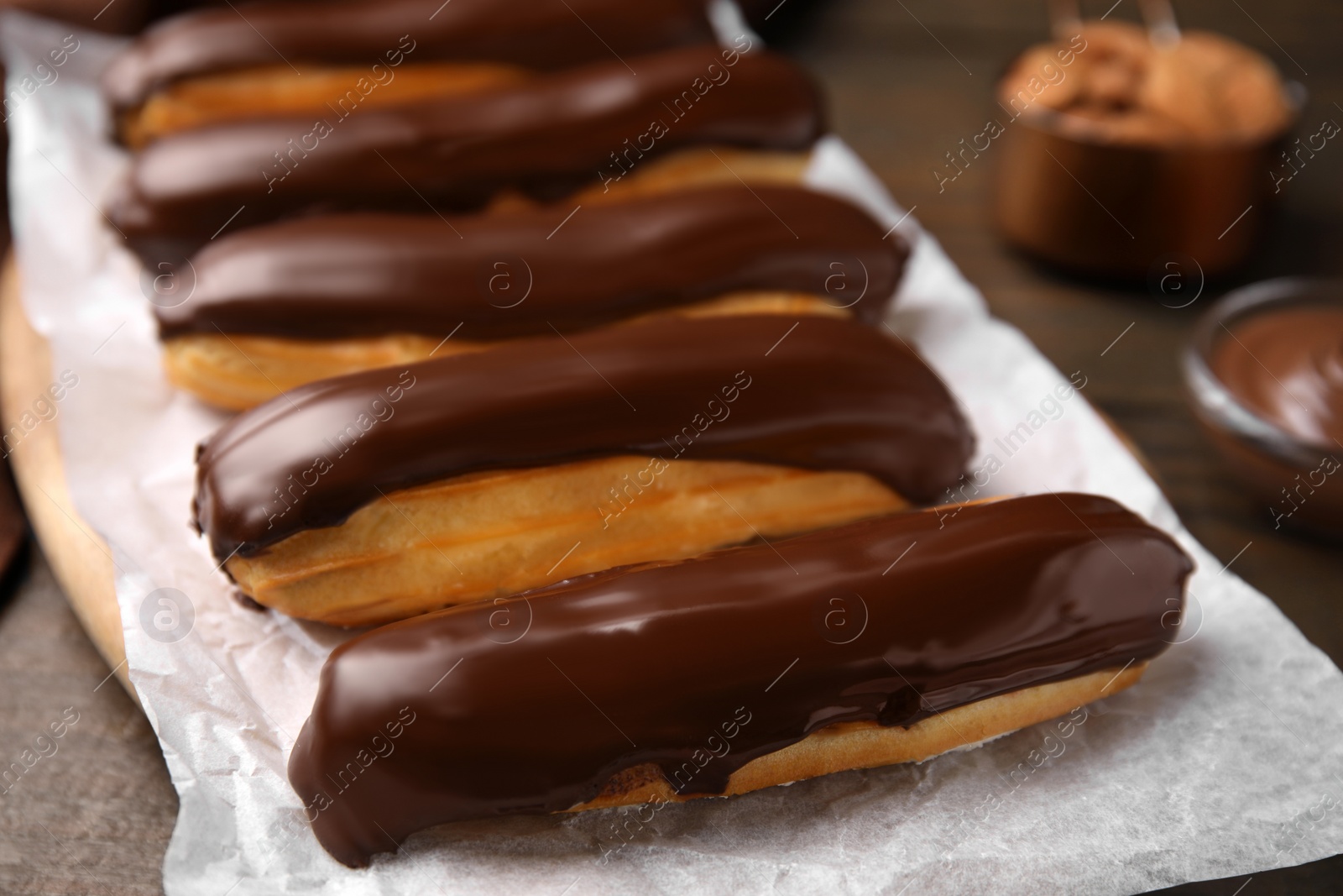 Photo of Delicious eclairs covered with chocolate on wooden table, closeup