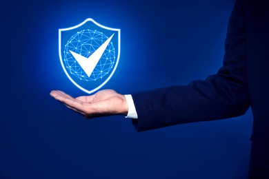 Image of Anti-fraud security system. Man with illustration of checkmark in shield on blue background, closeup