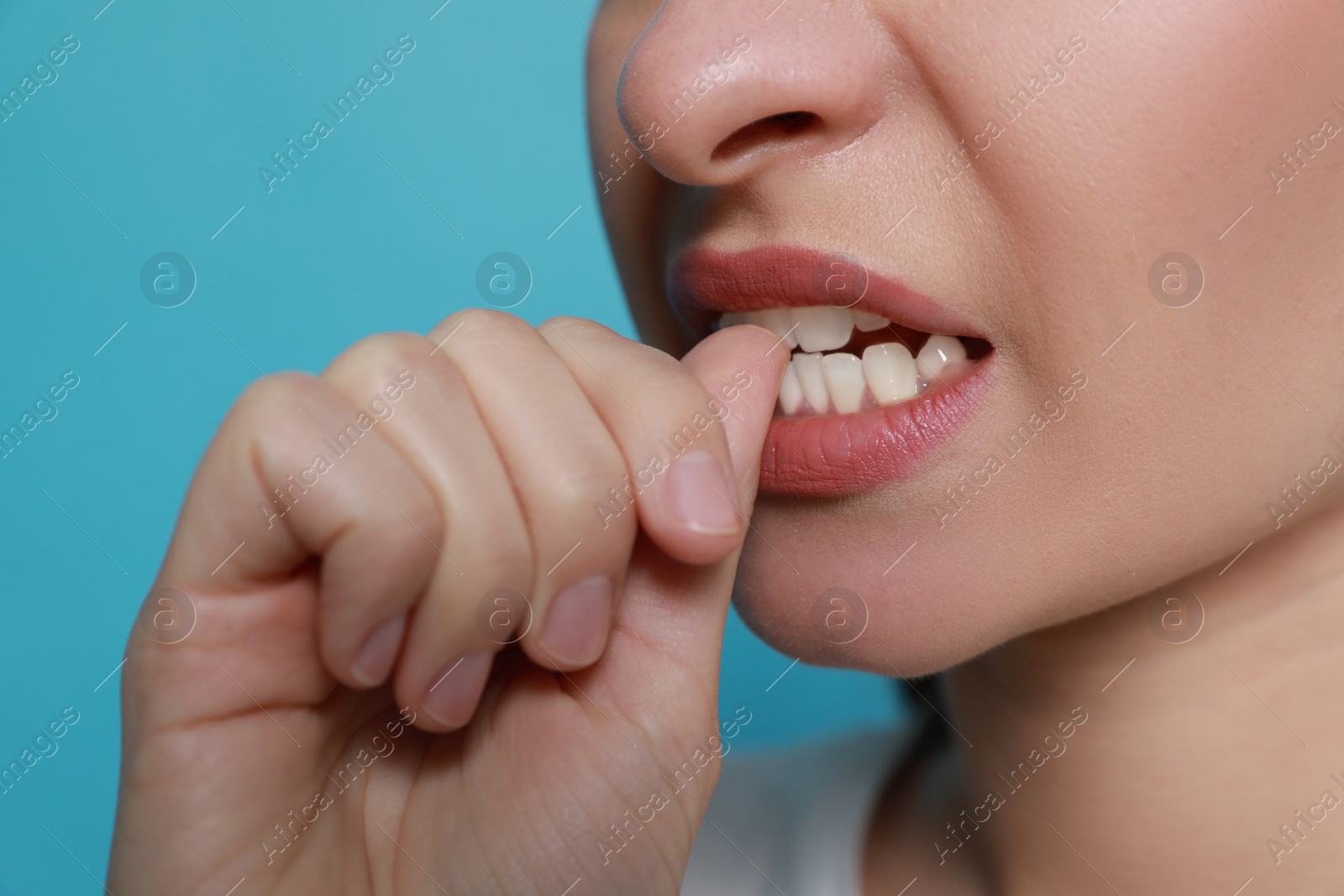 Photo of Young woman biting her nails on light blue background, closeup