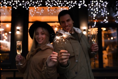 Happy couple with sparklers and glasses of champagne at winter fair