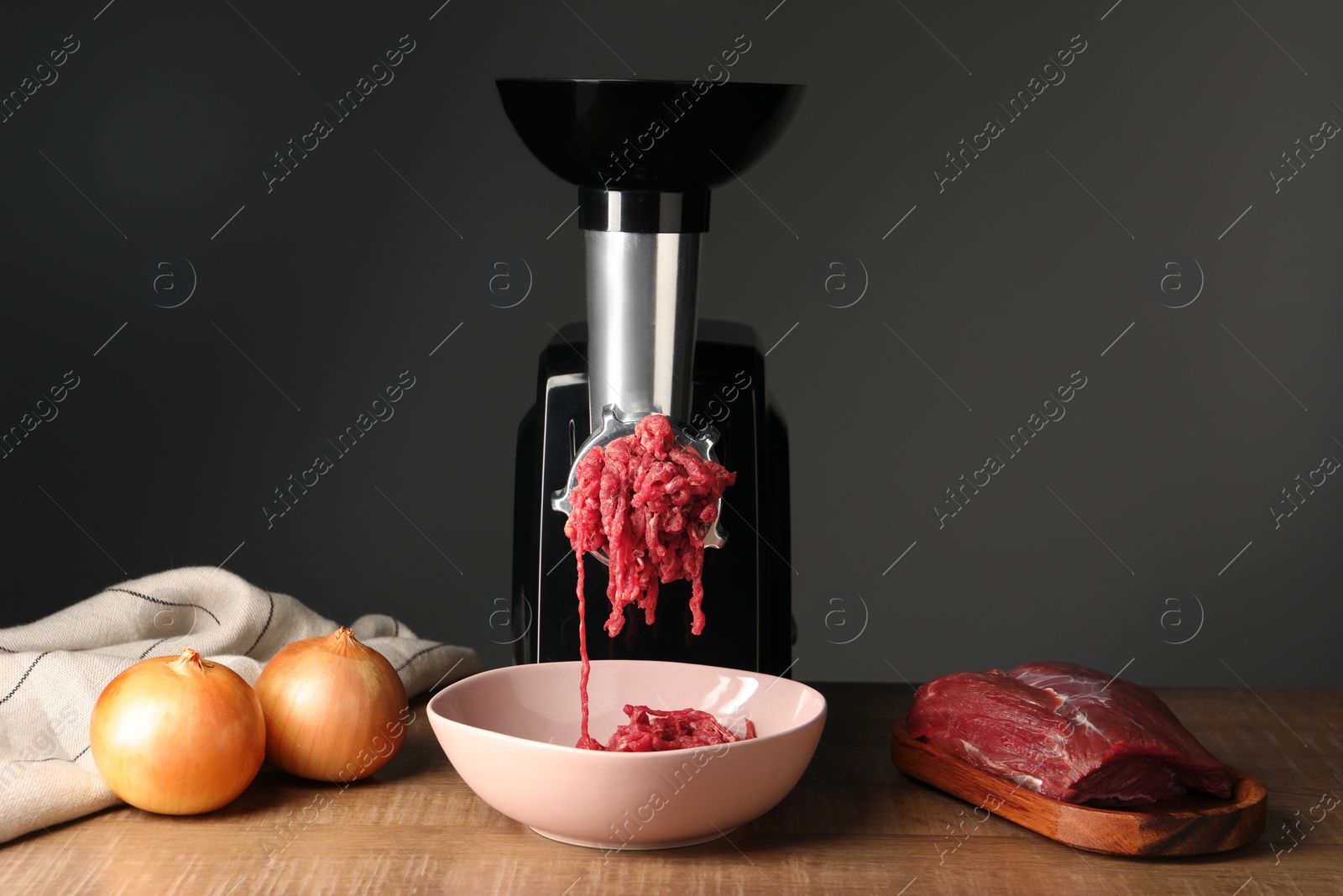 Photo of Electric meat grinder with beef mince and onion on wooden table against grey background