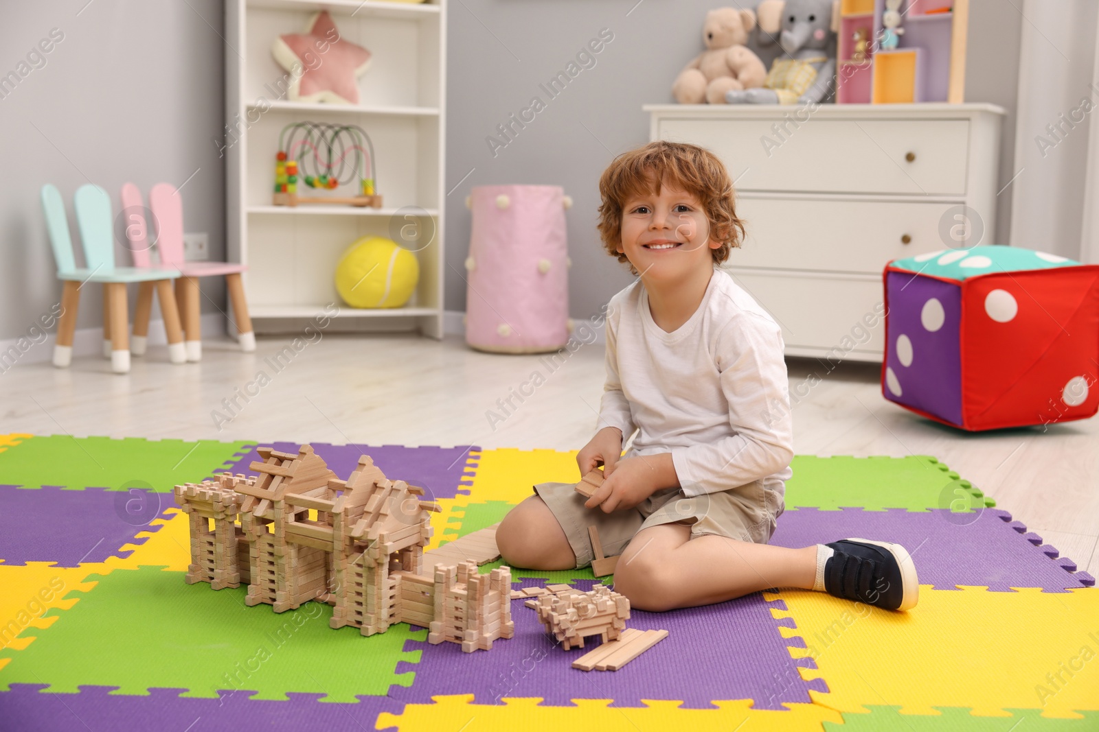 Photo of Little boy playing with wooden construction set on puzzle mat in room. Child's toy