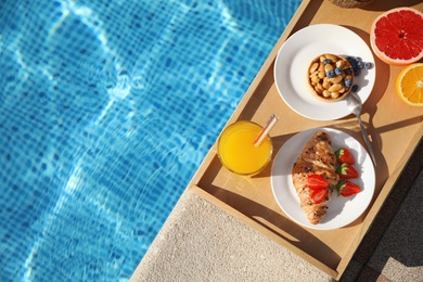 Photo of Tray with delicious breakfast near swimming pool, top view. Space for text