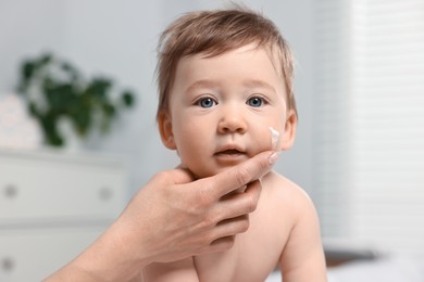 Mother applying moisturizing cream onto baby`s face indoors