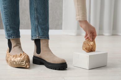 Photo of Woman wearing shoe covers onto her boots indoors, closeup