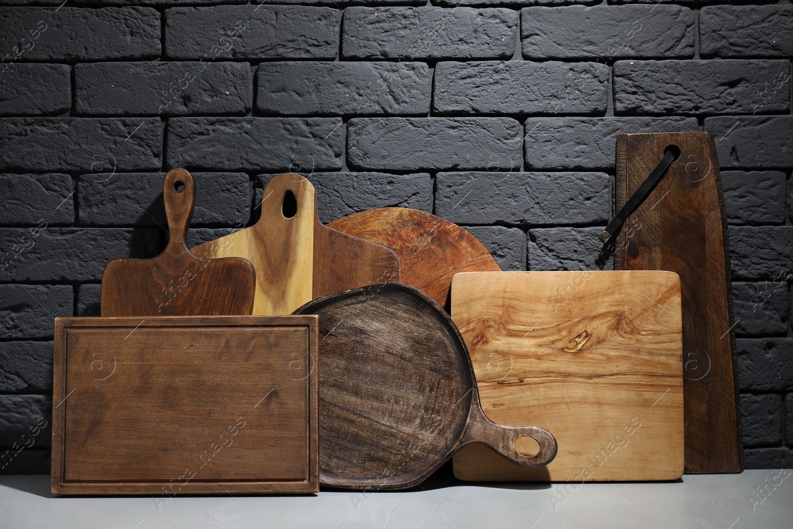 Photo of Different wooden cutting boards on gray table near dark brick wall