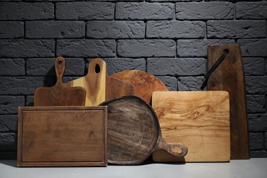 Photo of Different wooden cutting boards on gray table near dark brick wall
