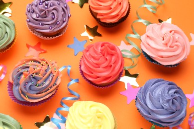 Photo of Delicious cupcakes with bright cream and party decor on orange background, flat lay