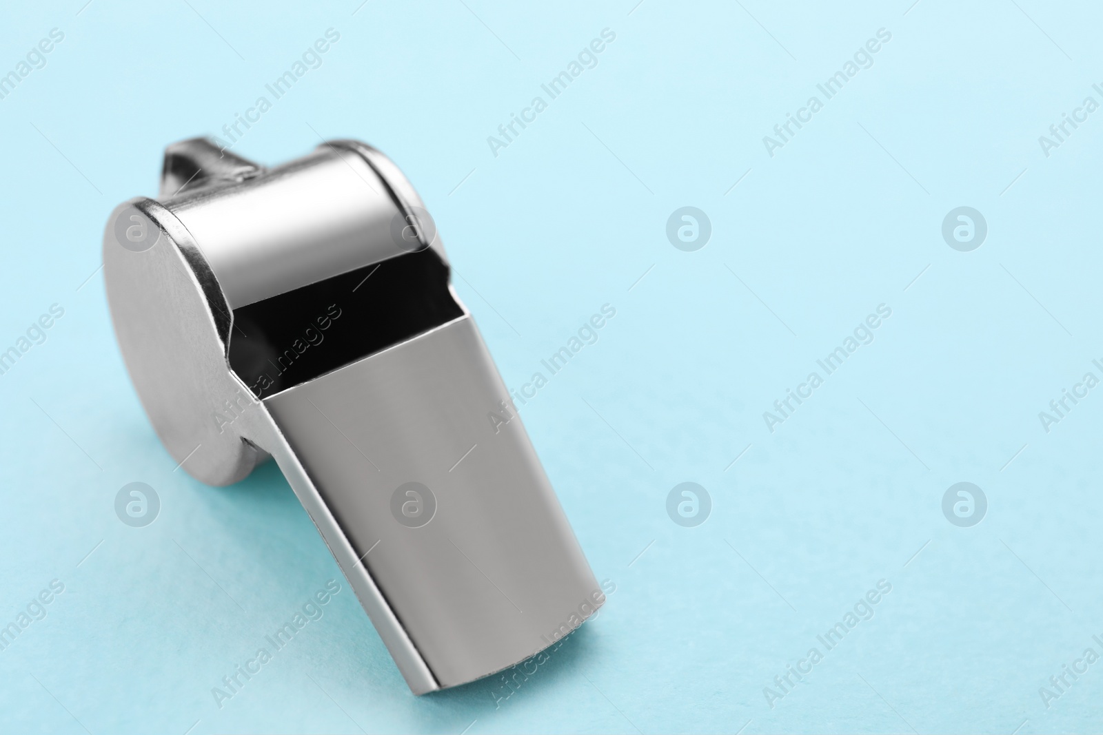 Photo of One metal whistle on light blue background, closeup. Space for text