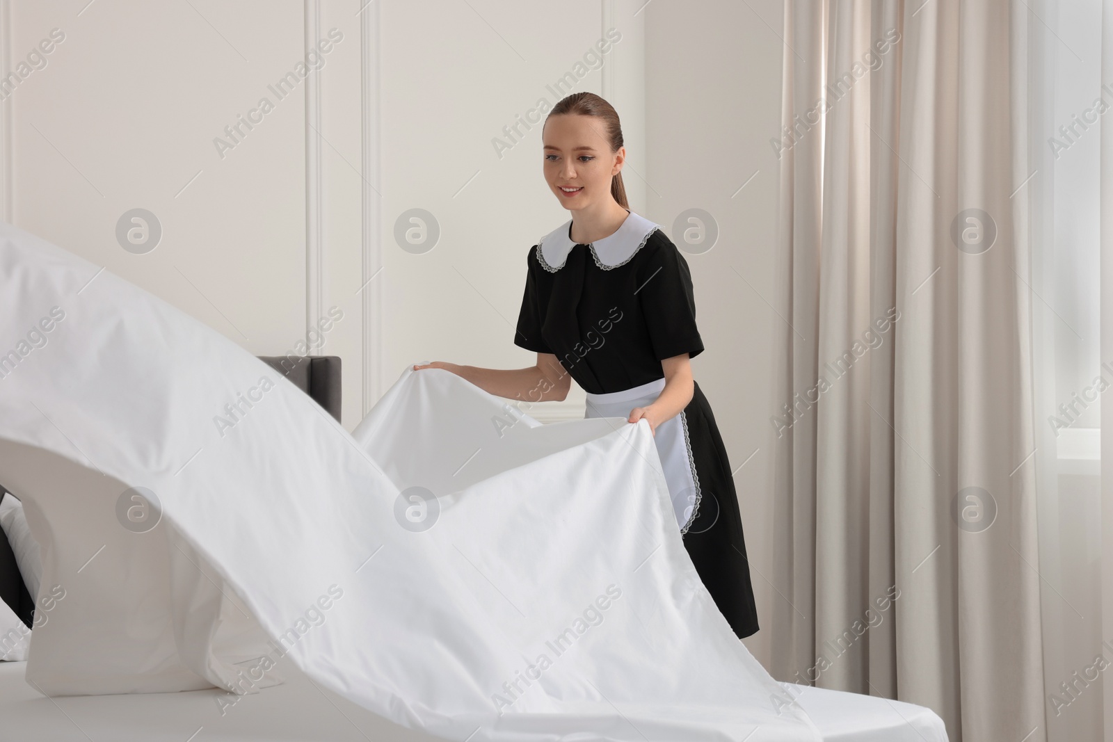 Photo of Young maid making bed in hotel room