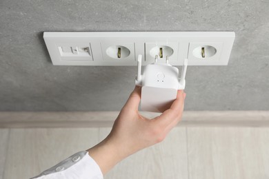 Woman inserting wireless Wi-Fi repeater into power socket indoors, above view