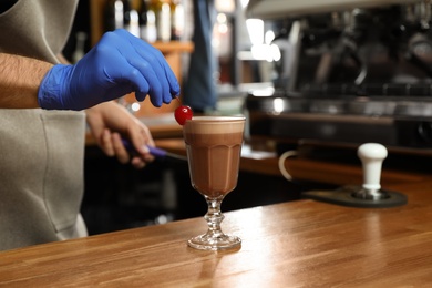 Photo of Barista decorating glass of coffee drink on bar counter, closeup