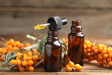 Photo of Natural sea buckthorn oil and fresh berries on wooden table
