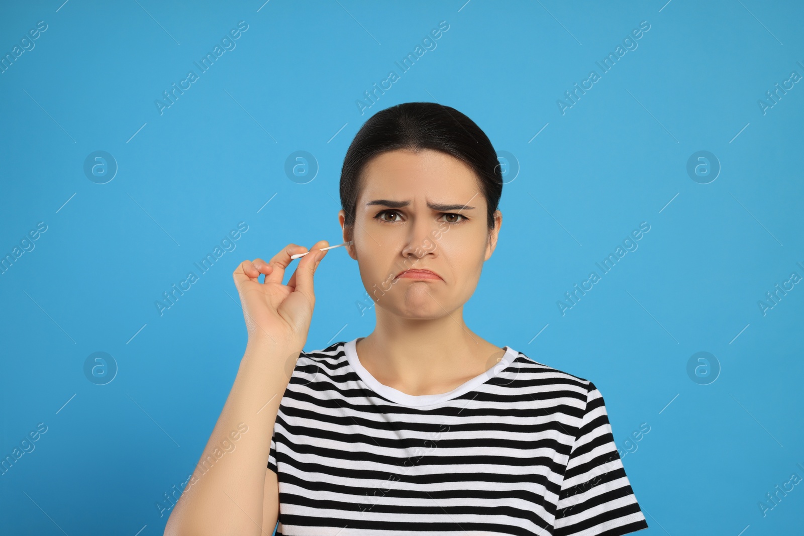 Photo of Young woman cleaning ear with cotton swab on light blue background