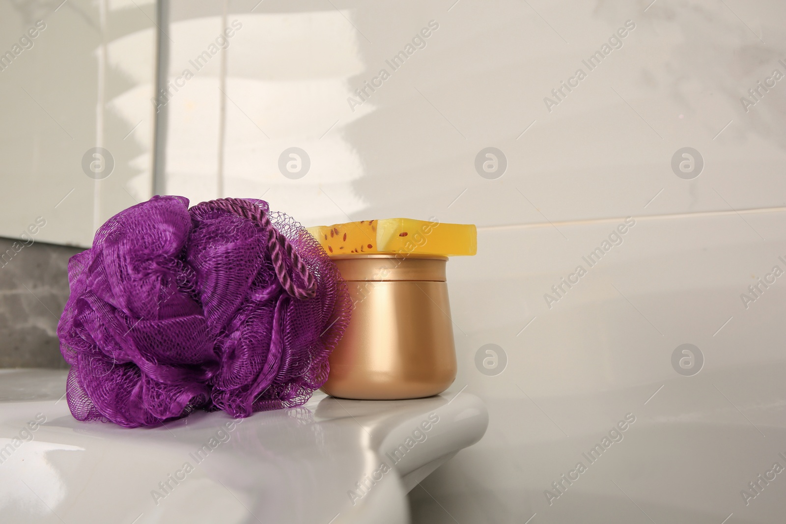 Photo of Purple shower puff and cosmetic products on sink in bathroom, space for text