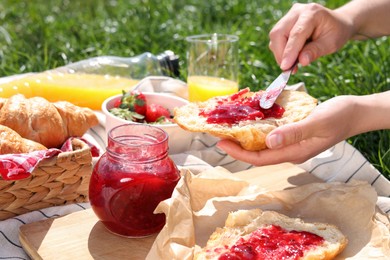 Photo of Woman spreading jam on croissant outdoors, closeup. Summer picnic