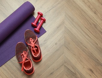 Photo of Dumbbells, sneakers and mat on wooden floor, above view. Space for text