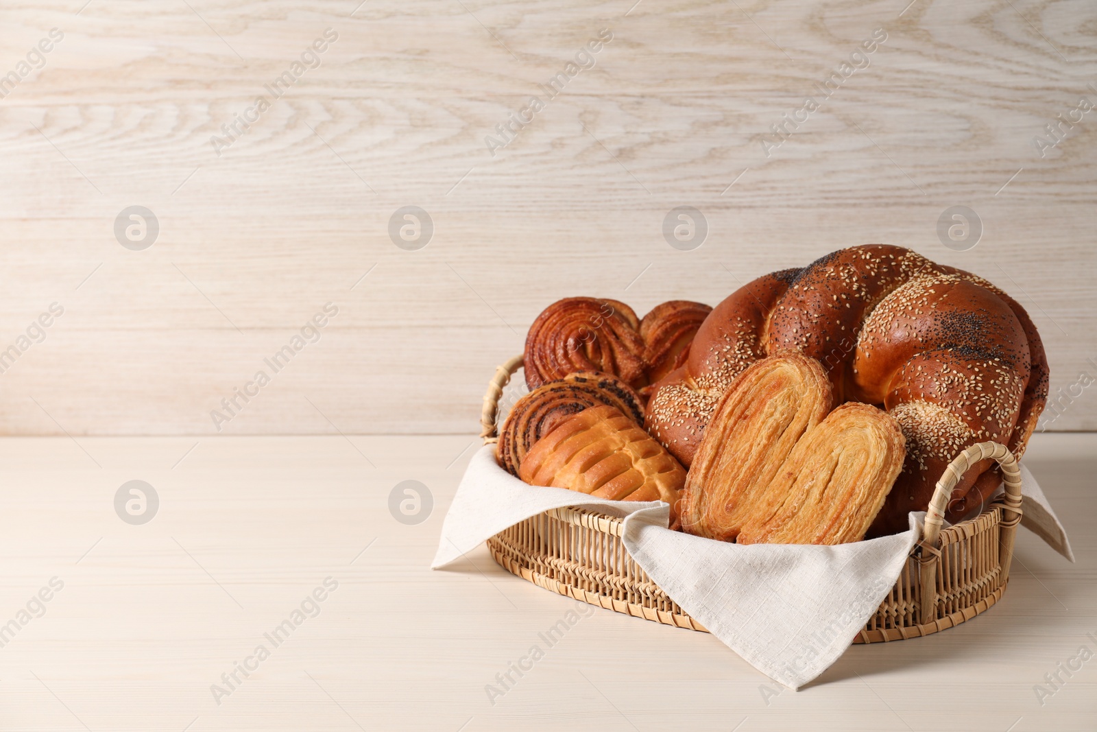 Photo of Wicker basket with different tasty freshly baked pastries on white table, space for text