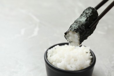 Photo of Chopsticks with cooked rice wrapped in nori sheet over light grey table, closeup. Space for text