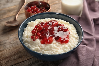 Photo of Creamy rice pudding with red currant and jam in bowl served on wooden table