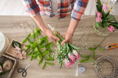 Male decorator creating beautiful bouquet at table, top view