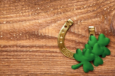 Golden horseshoe and decorative clover leaves on wooden table, flat lay with space for text. Saint Patrick's Day celebration