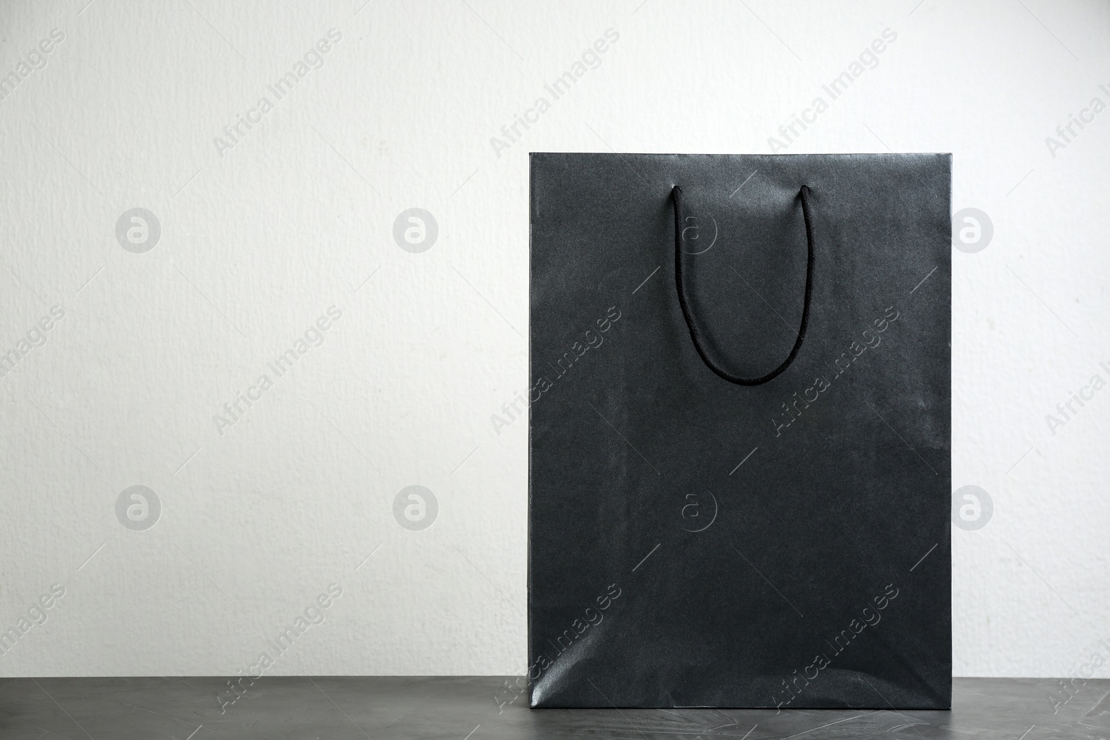 Photo of Black shopping paper bag on table against light background. Space for text