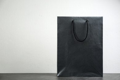 Black shopping paper bag on table against light background. Space for text