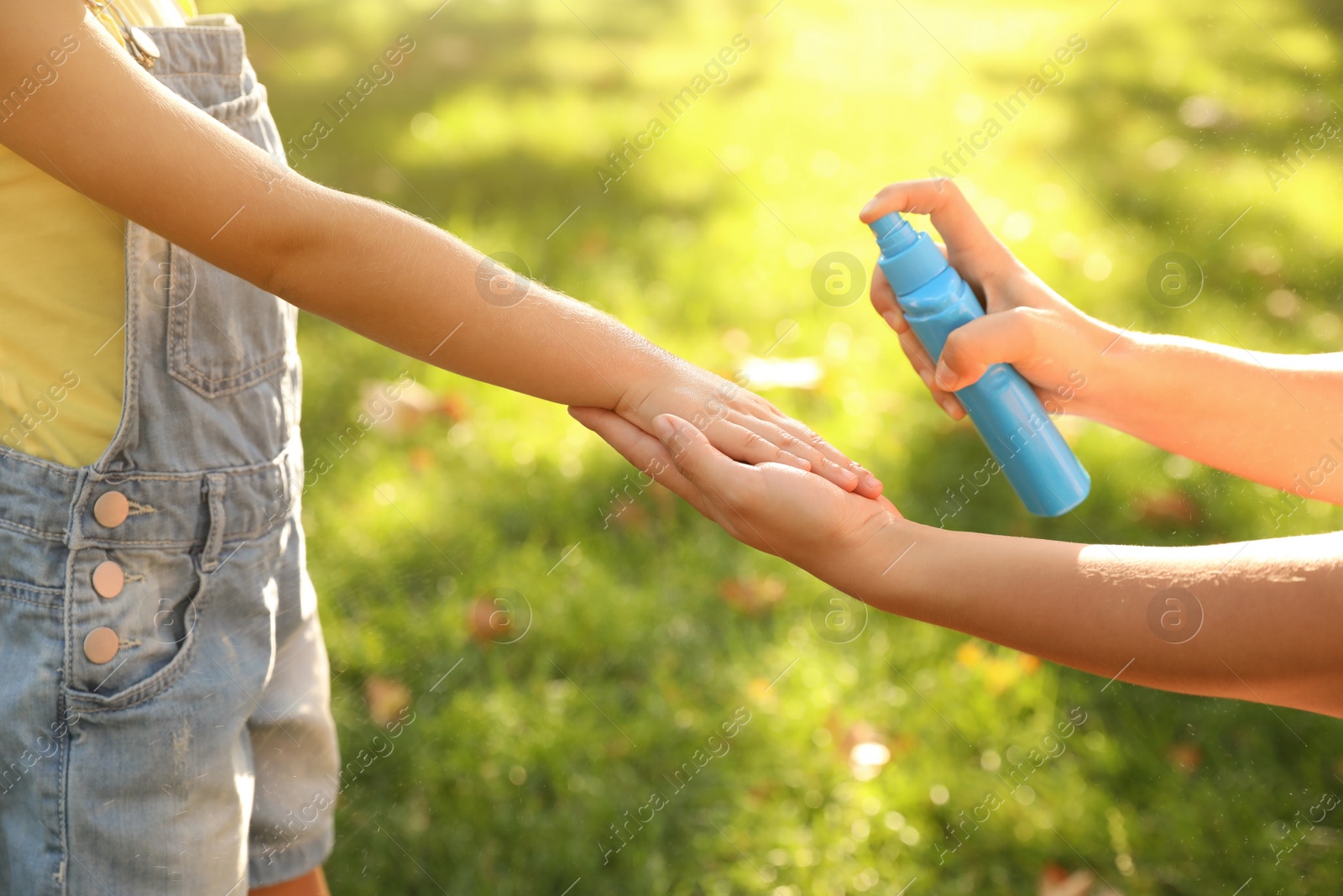 Photo of Mother applying insect repellent onto girl's hand in park, closeup