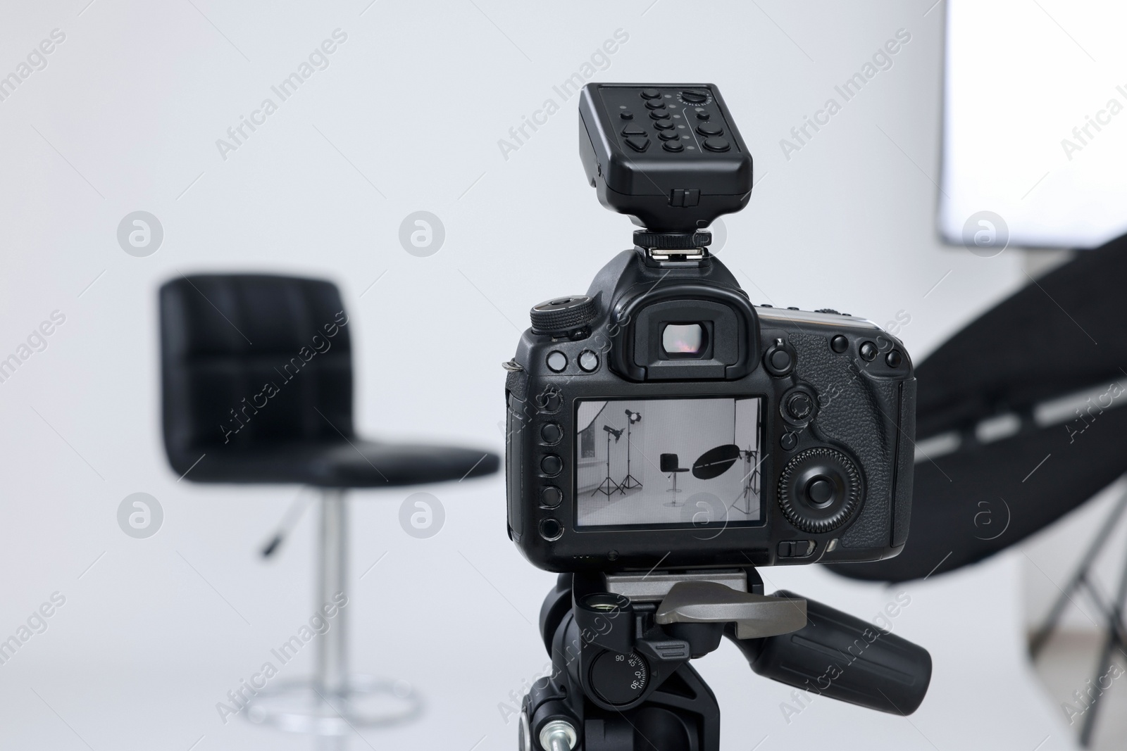 Photo of Tripod with camera, bar stool and professional lighting equipment in modern photo studio, focus on screen. Space for text