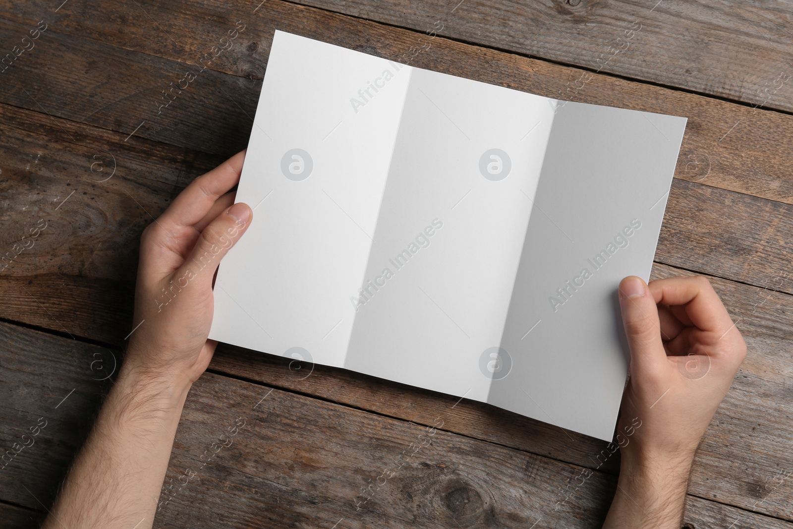 Photo of Man with blank brochure on wooden background, above view. Mock up for design