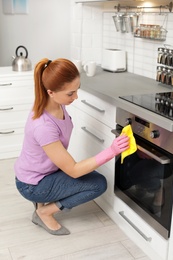 Woman cleaning modern oven with rag in kitchen