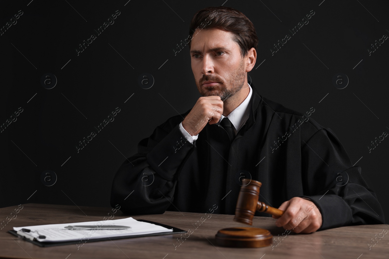 Photo of Judge with gavel and papers sitting at wooden table against black background